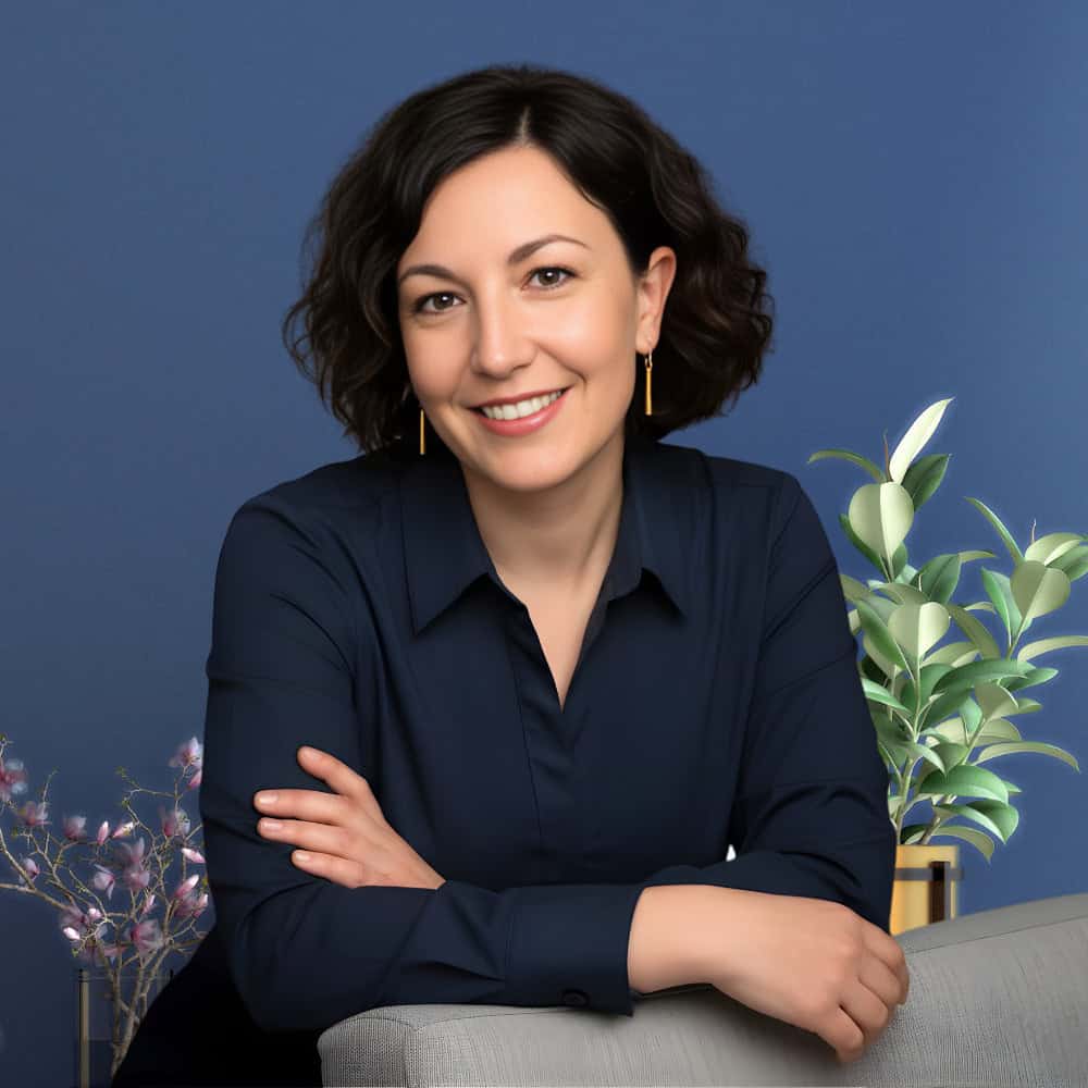 Frau lehnt auf einem Stuhl, lacht freundlich in die Kamera. 